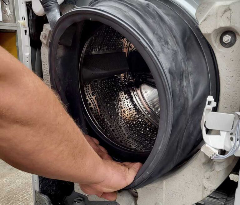 Techniker zieht an der Türabdichtung einer aufgeschraubten Waschmaschine