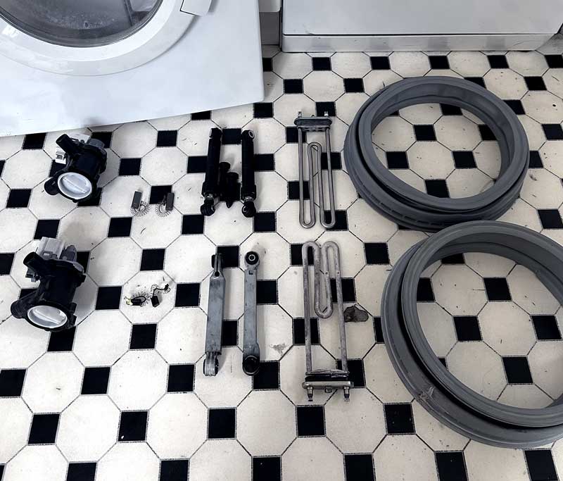 Gebrauchte und neue Ersatzteile einer Waschmaschine auf dem Boden jeweils gegenübergestellt