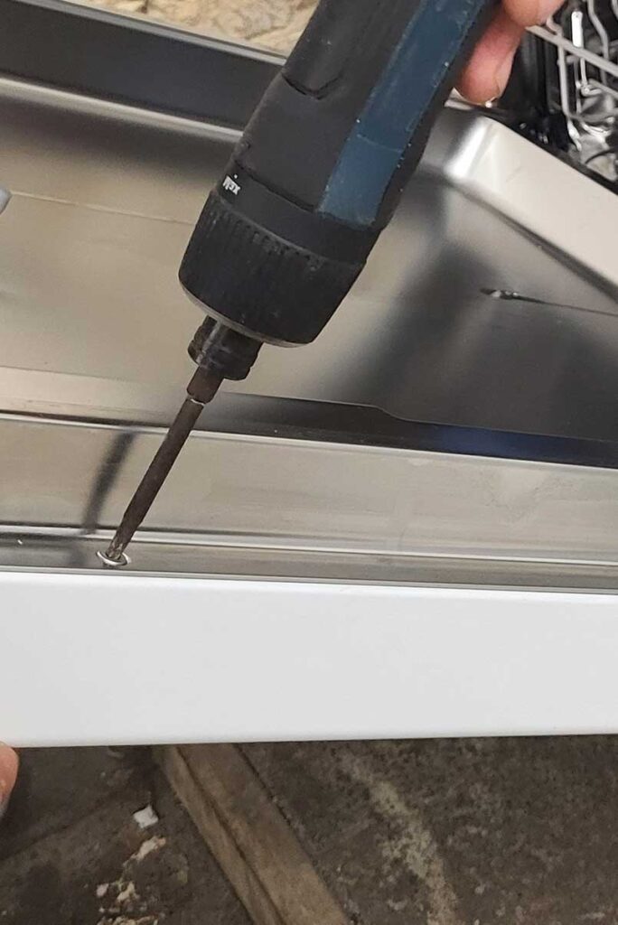 Schraubenzieher wird an eine geöffnete Geschirrspülertür gehalten.