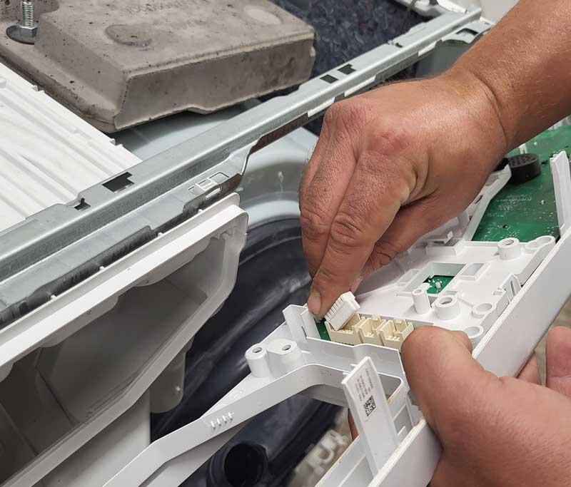 Abgeschraubtes Bedienelement einer Waschmaschine, Techniker hält ein Ersatzteil