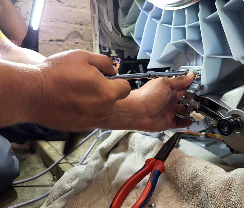 Techniker arbeiten an der Rückseite einer aufgeschraubten Waschmaschine