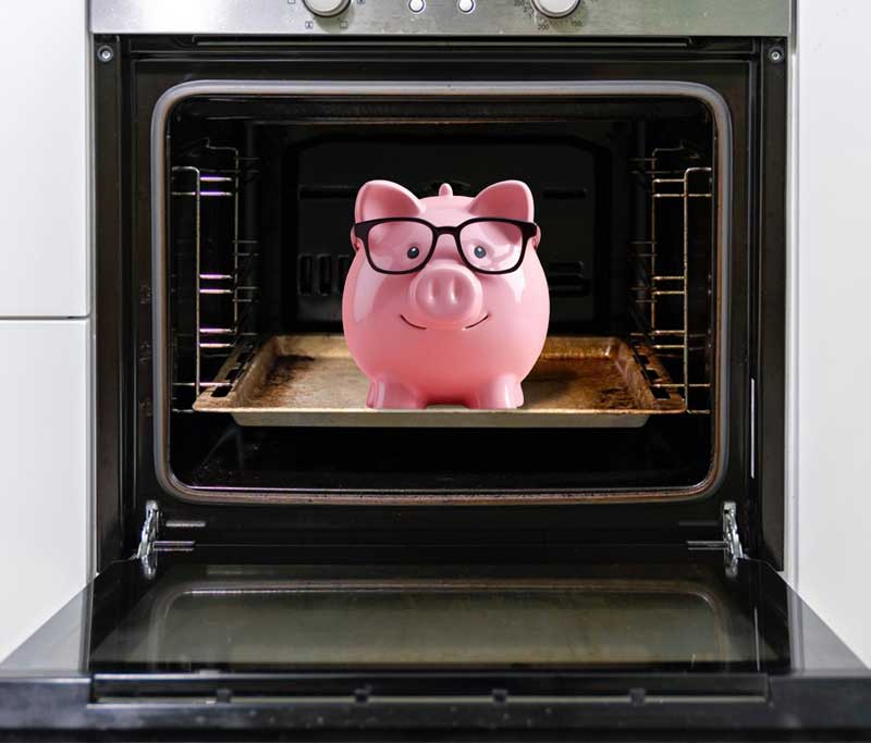 Sparschwein mit Brille auf einem Backblech in einem Backofen