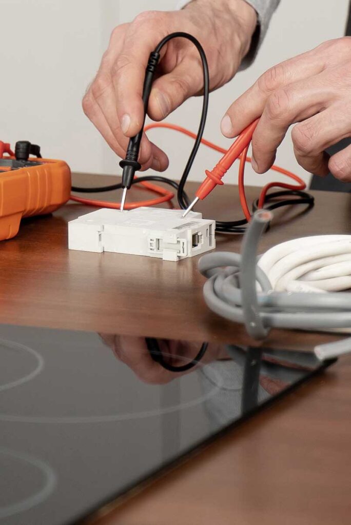 Prüfung eines Ersatzteils mit einem Elektromessgerät neben Kochfeldern