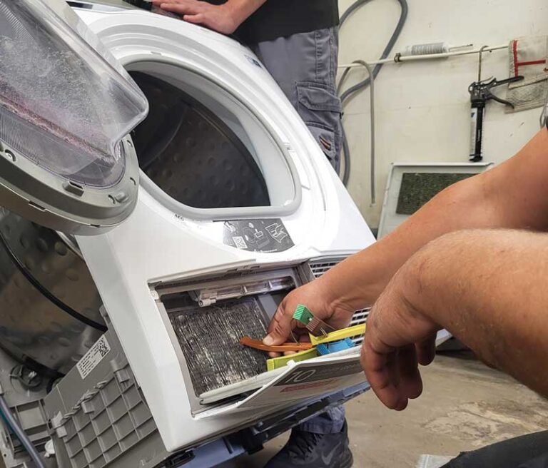 Ein Techniker winkelt einen Wäschetrockner an, ein anderer Techniker arbeitet daran