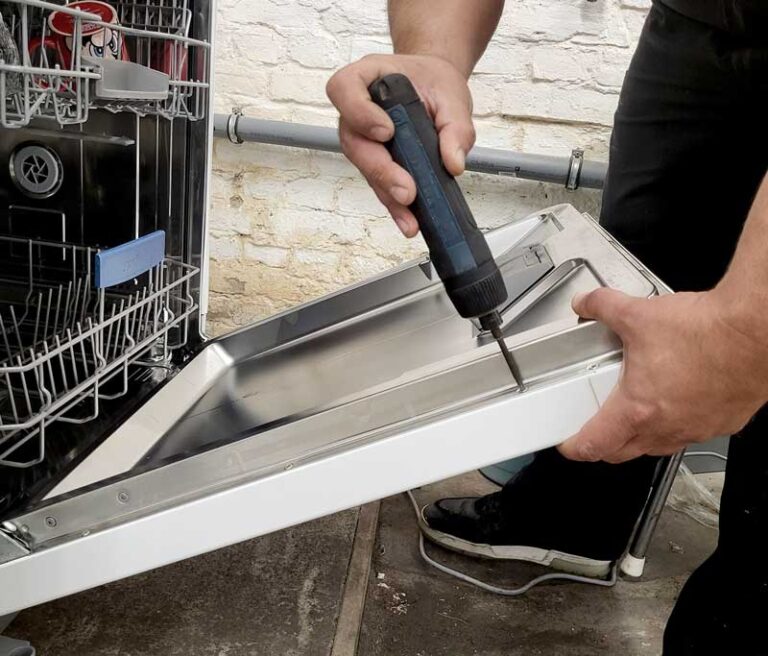 Techniker hält geöffnete Geschirrspülertür und schraubt an ihr