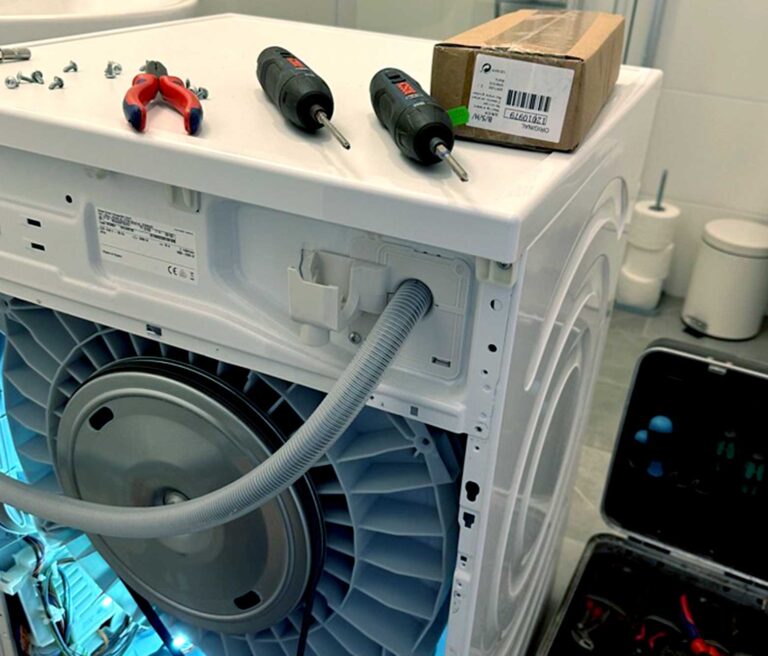 Aufgeschraubte Rückseite einer Waschmaschine, auf der Waschmaschine befinden sich Werkzeuge