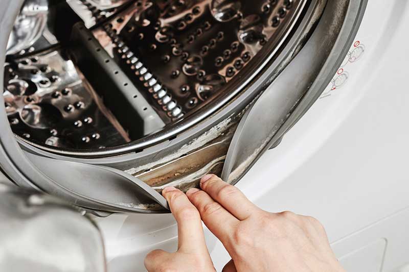 Drei Finger spreizen die Türdichtung einer Waschmaschine auf.
