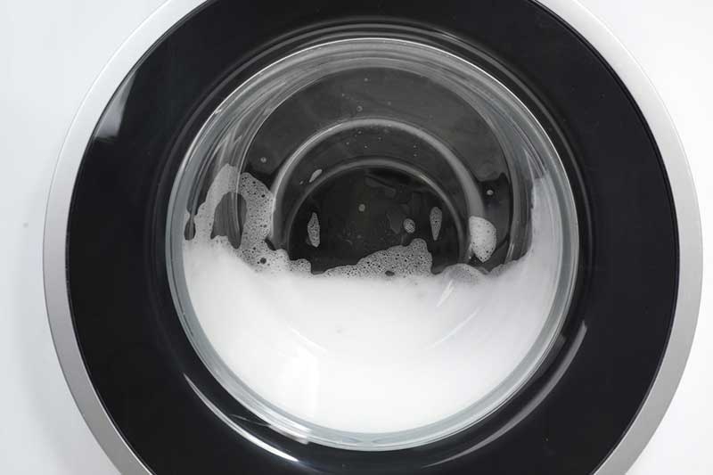 Nahaufnahme: Waschmachinenfenster das halb mit Schaum gefüllt ist