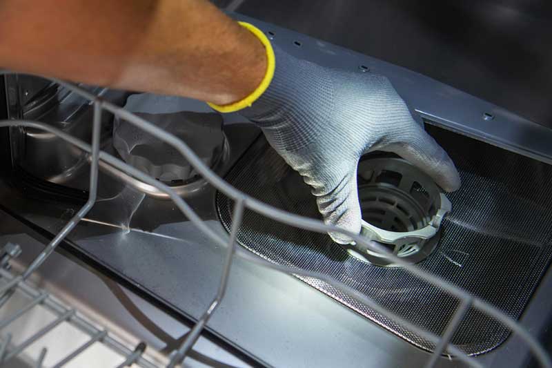 Im Inneren eines Geschirrspülers hält eine Hand mit Handschuh den Filter