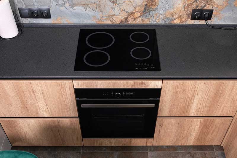 Draufsicht auf eine moderne Küchenzeile in Holzoptik mit einem schwarzen Induktionskochfeld und einem darunter eingebauten Backofen.