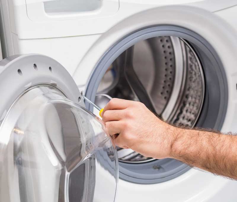 Nahaufnahme eines Reparaturvorgangs an der Türdichtung einer weißen Frontlader-Waschmaschine mithilfe eines Schraubendrehers.