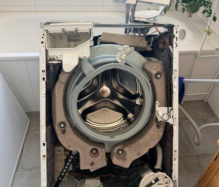 Aufgeschraubte Waschmaschine vor einer Badewanne.