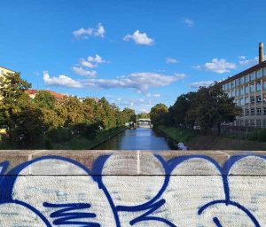 Ein Teil einer Brücke, dahinter sieht man den Landwehrkanal mit Bäumen an den Ufern