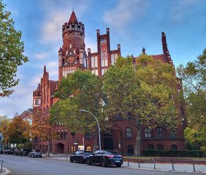 Rathaus Schmargendorf: Neugotisches historisches Gebäude aus rotem Backstein mit reich verziertem Uhrenturm und Erkern, umgeben von Herbstbäumen und geparkten Autos.
