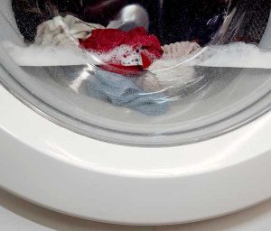 Nahaufnahme Glasauge Waschmaschine, halb gefüllt mit Wasser und Kleidungsstücken